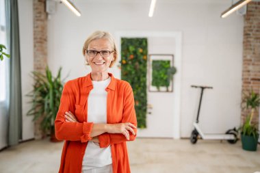Ofiste gözlüklü, olgun, beyaz bir kadının portresi. Mutlu bir gülümseme. Kendine güvenen fotoğraf makinesine bakıyor.