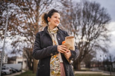 Bir kadının portresi organik meyve ve sebzeleri kesekağıdında tutuyor.