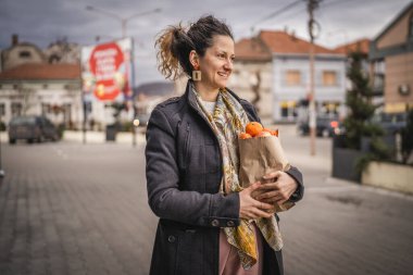 Bir kadının portresi organik meyve ve sebzeleri kesekağıdında tutuyor.