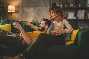 Birkaç beyaz erkek ve kadın evlerinde kanepede film izliyorlar.