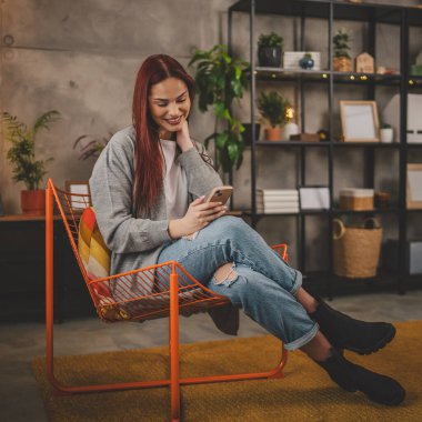 Evde genç bir kadın cep telefonu mesajlaşması kullanıyor ya da internette geziniyor