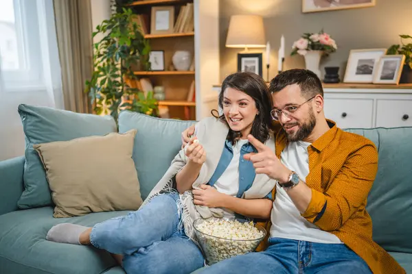 Kafkasyalı bir erkek ve kadın, evlerinde kanepede oturup televizyon seyrediyorlar.