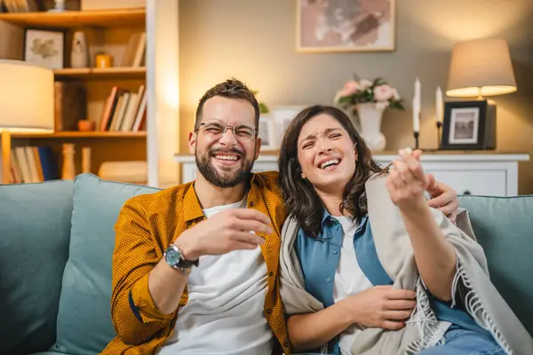 Kafkasyalı bir erkek ve kadın, evlerinde kanepede oturup televizyon seyrediyorlar.
