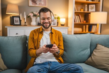 Yetişkin bir adam akıllı telefonuyla evde mutlu bir gülümseme ile şarkı söyler.