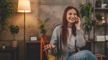 Evdeki bir genç kadın cep telefonu kullanıyor. Akıllı telefon konuşuyor.