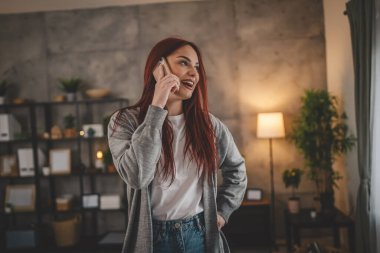 Evdeki bir genç kadın cep telefonu kullanıyor. Akıllı telefon konuşuyor.