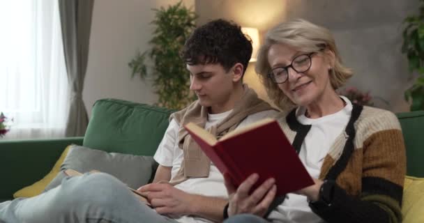 母亲和十几岁的儿子男人和女人坐在家里沙发床上看书 — 图库视频影像