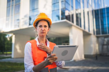 Mimar kadın inşaat mühendisi dışarıda duruyor ve modern bina duvarının önünde koruyucu başlık takıyor.