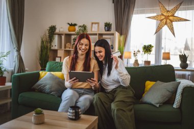 İki genç kız kardeş ya da arkadaş evlerinde oturup online alışveriş için kredi kartı kullanıyorlar dijital tablette internet mağazaları satın alıyorlar indirimli eşya satışı yapıyorlar gerçek insanlar boşluğu kopyalıyorlar