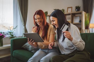 İki genç kız kardeş ya da arkadaş evlerinde oturup online alışveriş için kredi kartı kullanıyorlar dijital tablette internet mağazaları satın alıyorlar indirimli eşya satışı yapıyorlar gerçek insanlar boşluğu kopyalıyorlar