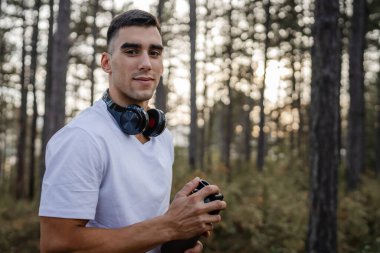 Kafkas kökenli genç bir erkek sporcu açık havada, ormandaki parkta ya da doğadaki ormanlık alanda çalışırken fren yapıyor. Elinde güçlü ve mutlu bir kopya alanı tutuyor.