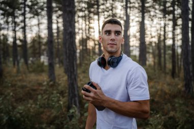 Kafkas kökenli genç bir erkek sporcu açık havada, ormandaki parkta ya da doğadaki ormanlık alanda çalışırken fren yapıyor. Elinde güçlü ve mutlu bir kopya alanı tutuyor.
