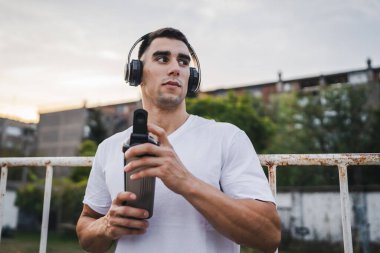 Beyaz tenli genç bir erkek sporcu açık hava eğitimi sırasında fren yapıyor. Elinde destek aleti tutuyor. Kendine güveni tam, güçlü bir kopya alanı.