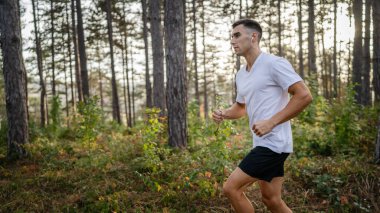 Kafkasyalı genç bir erkek sporcu doğada ormanda koşuyor sonbaharda ya da yazın koşuyor spor yapıyor spor yapıyor sağlıklı yaşam tarzı kavramı gerçek insanlar mekanı kopyalıyor.