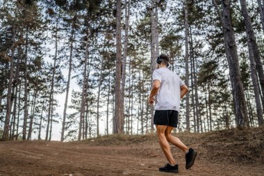 Kafkasyalı genç bir erkek sporcu doğada ormanda koşuyor sonbaharda ya da yazın koşuyor spor yapıyor spor yapıyor sağlıklı yaşam tarzı kavramı gerçek insanlar mekanı kopyalıyor.