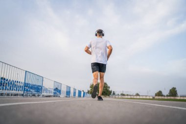 Koşu parkurunda koşan beyaz bir adam. Stadyum erkek sporcusu. Güneşli bahar ve yaz günlerinde koşuyor.