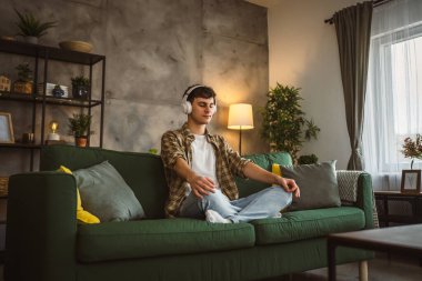 Rehberli meditasyon yapan genç bir adam evde yoga yapıyor.