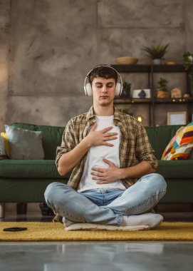 Rehberli meditasyon yapan genç bir adam evde yoga yapıyor.