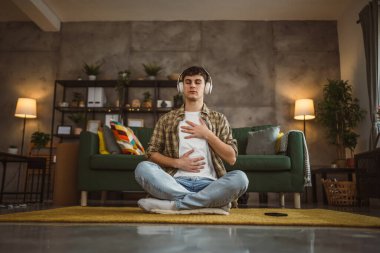 Rehberli meditasyon yapan genç bir adam evde yoga yapıyor.