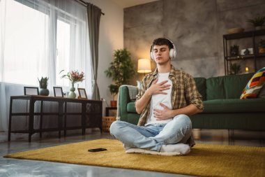 Rehberli meditasyon yapan genç bir adam evde yoga yapıyor.