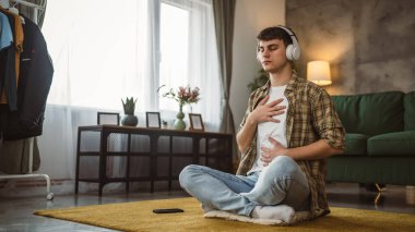 Rehberli meditasyon yapan genç bir adam evde yoga yapıyor.