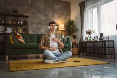 Rehberli meditasyon yapan genç bir adam evde yoga yapıyor.