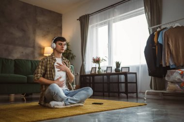 Rehberli meditasyon yapan genç bir adam evde yoga yapıyor.