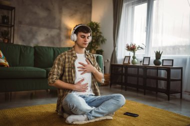 Rehberli meditasyon yapan genç bir adam evde yoga yapıyor.