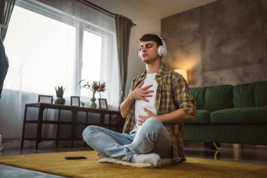 Rehberli meditasyon yapan genç bir adam evde yoga yapıyor.