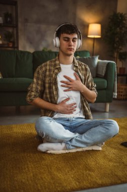 Rehberli meditasyon yapan genç bir adam evde yoga yapıyor.