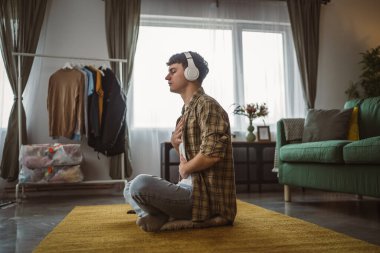 Rehberli meditasyon yapan genç bir adam evde yoga yapıyor.