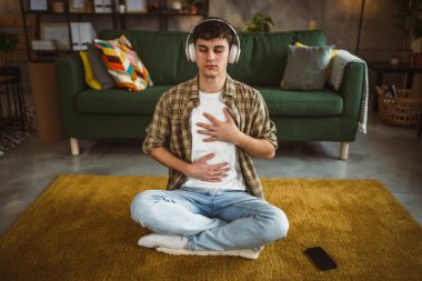 Rehberli meditasyon yapan genç bir adam evde yoga yapıyor.