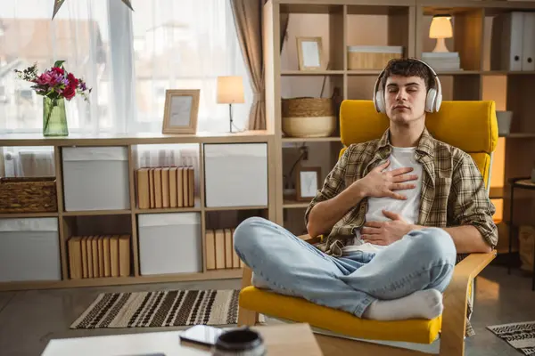 Rehberli meditasyon yapan genç bir adam evde yoga yapıyor.