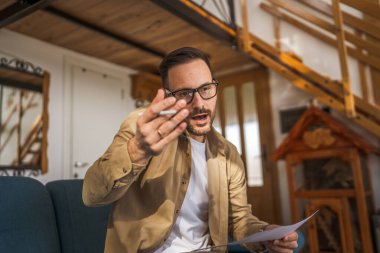 Evden çalışan yetişkin bir beyaz adam kanepeye oturur telefon görüşmesi yapar. Bu arada evraklar, iş raporları ya da belgeler elinde olur.