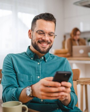 Gözlüklü adam evde duruyor. Cep telefonu mesajlaşması kullan.