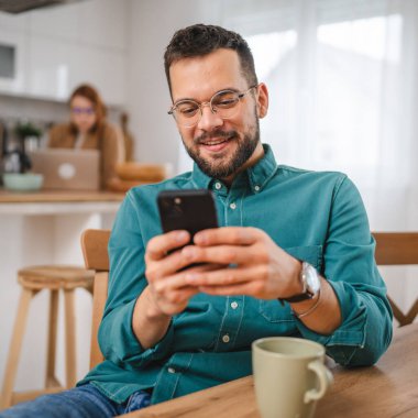 Gözlüklü adam evde duruyor. Cep telefonu mesajlaşması kullan.