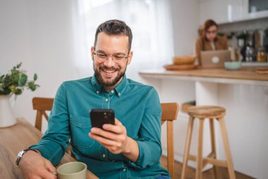 Gözlüklü adam evde duruyor. Cep telefonu mesajlaşması kullan.