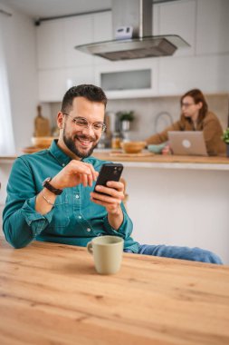 Gözlüklü adam evde duruyor. Cep telefonu mesajlaşması kullan.