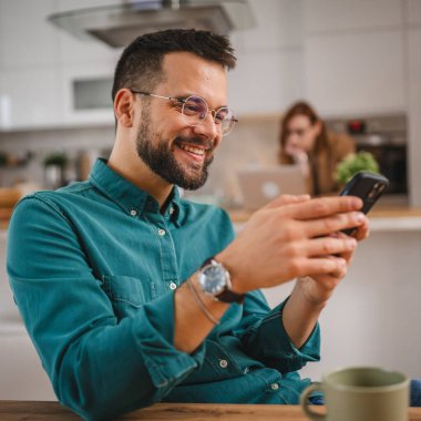 Gözlüklü adam evde duruyor. Cep telefonu mesajlaşması kullan.