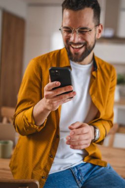 Gözlüklü adam evde duruyor. Cep telefonu mesajlaşması kullan.