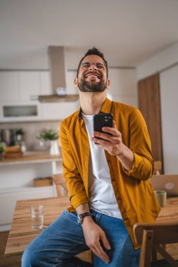 Gözlüklü adam evde duruyor. Cep telefonu mesajlaşması kullan.