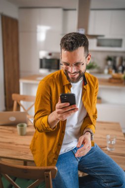 Gözlüklü adam evde duruyor. Cep telefonu mesajlaşması kullan.