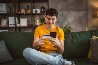 Evdeki genç adam internette kredi kartı alışverişi yapıyor.