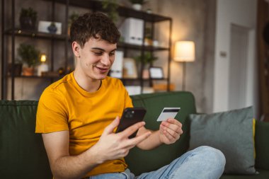 Evdeki genç adam internette kredi kartı alışverişi yapıyor.