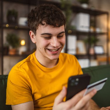 Evdeki genç adam internette kredi kartı alışverişi yapıyor.