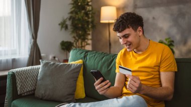 Evdeki genç adam internette kredi kartı alışverişi yapıyor.