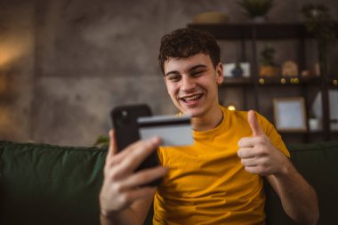 Evdeki genç adam internette kredi kartı alışverişi yapıyor.