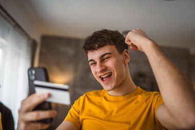 Evdeki genç adam internette kredi kartı alışverişi yapıyor.