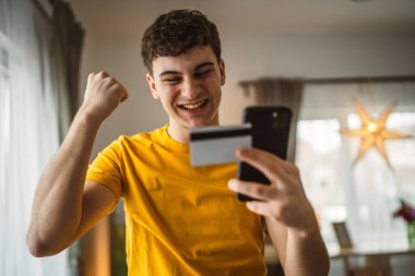 Evdeki genç adam internette kredi kartı alışverişi yapıyor.