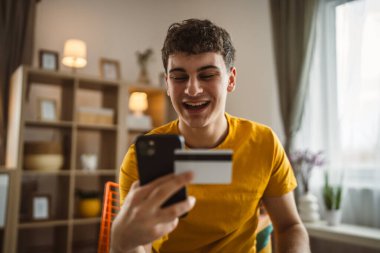 Evdeki genç adam internette kredi kartı alışverişi yapıyor.